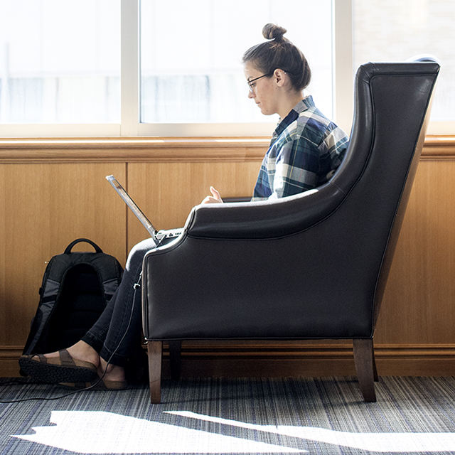 In profile, a female TCU student writes on a laptop next to a window in Rees-Jones Hall.