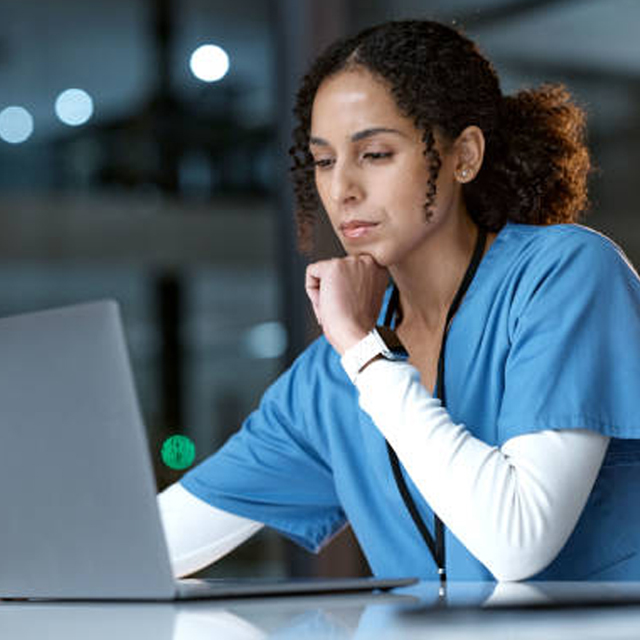 Medical professional in scrubs leaning over table to view laptop screen